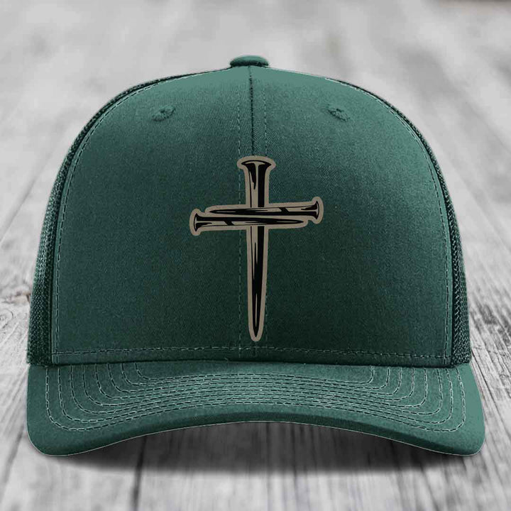 Grey trucker hat with black cross of nails patch on front, placed on wooden surface.
