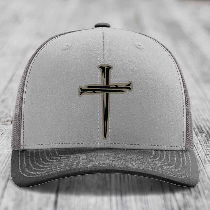 Grey and beige trucker hat with black cross of nails patch on front.