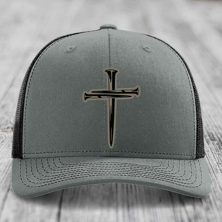 Grey trucker hat with black cross of nails patch on front, white mesh back and stitching.