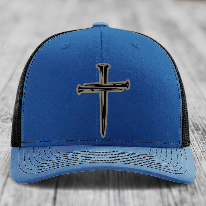 Blue and red trucker hat with a cross made of nails patch on front.