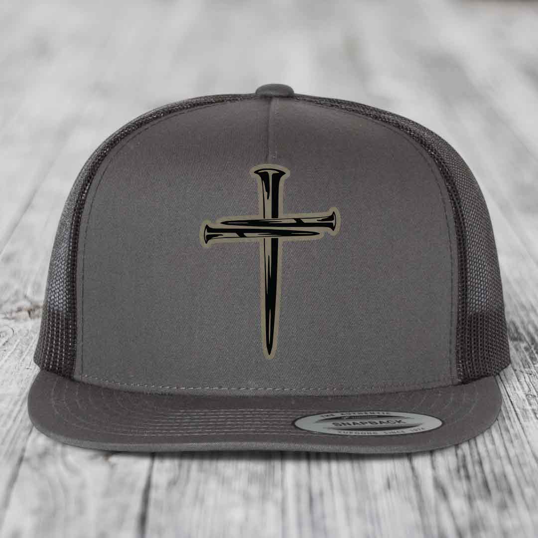 Grey trucker hat with black cross of nails patch on front, black mesh back, and Flexfit label.