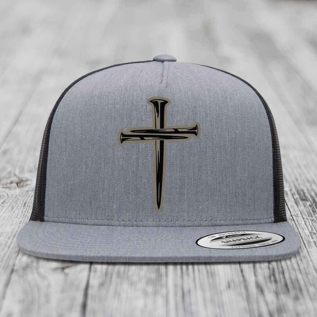 Grey trucker hat with black cross of nails patch on front, white mesh back, and snapback closure.
