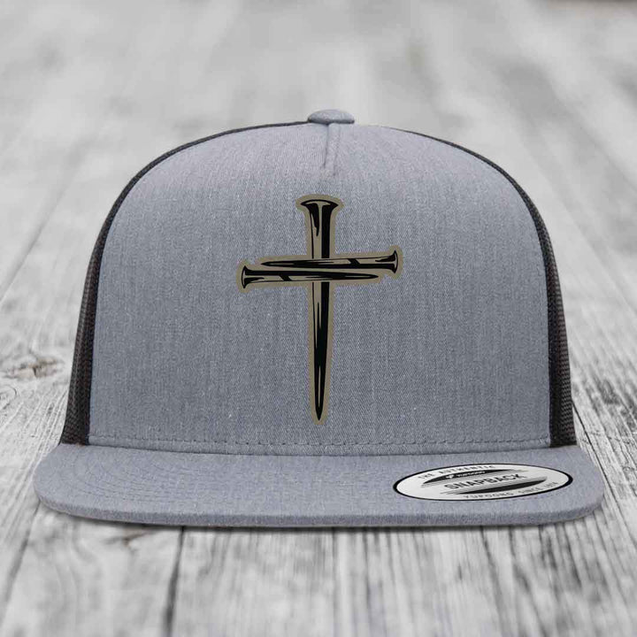 Grey trucker hat with black cross of nails patch on front, white mesh back, and snapback closure.