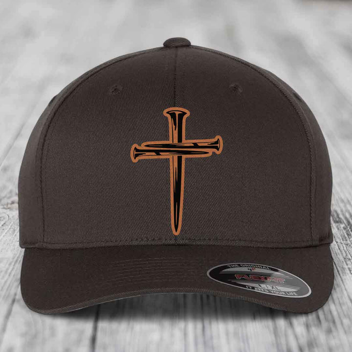 Beige baseball cap with a cross of nails patch on front, displayed on wooden surface.
