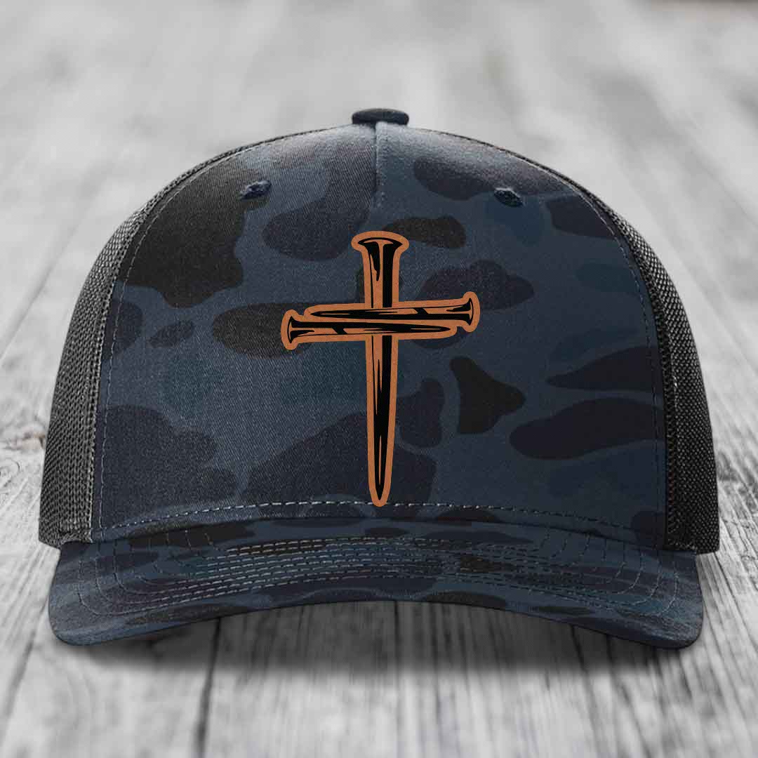Camouflage trucker hat with a cross made of nails patch on front.