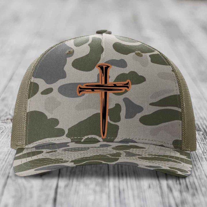 Camouflage trucker hat with a cross made of nails patch on front.