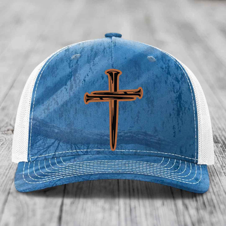 Camouflage trucker hat with orange cross of nails patch on front.