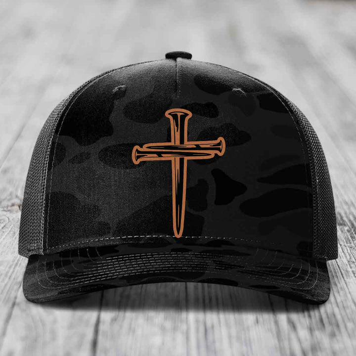 Camouflage trucker hat with a cross made of nails patch on front.