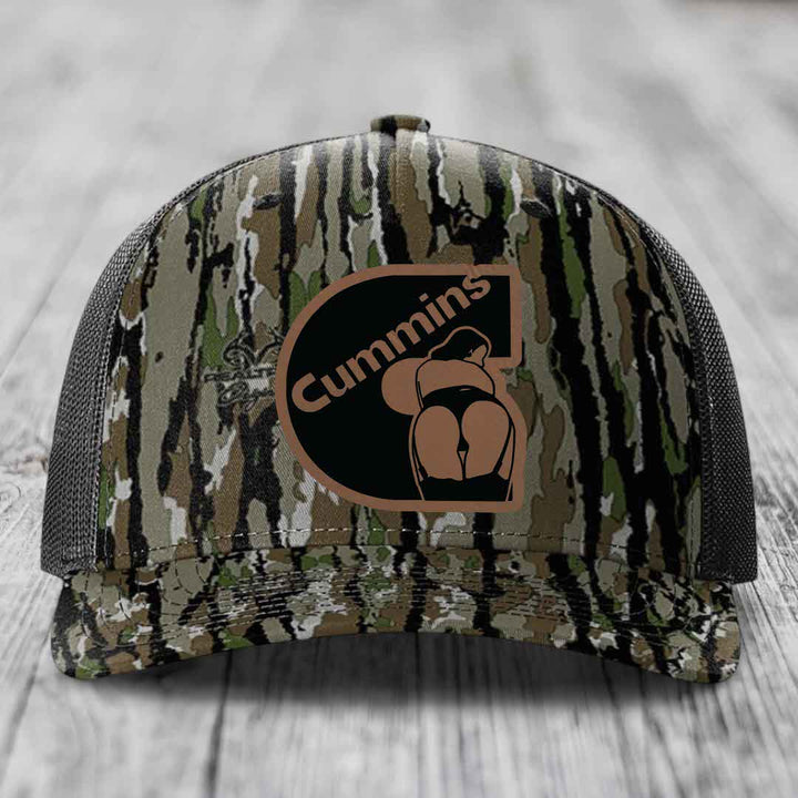 Black camouflage trucker hat with brown Cummins logo patch on front.