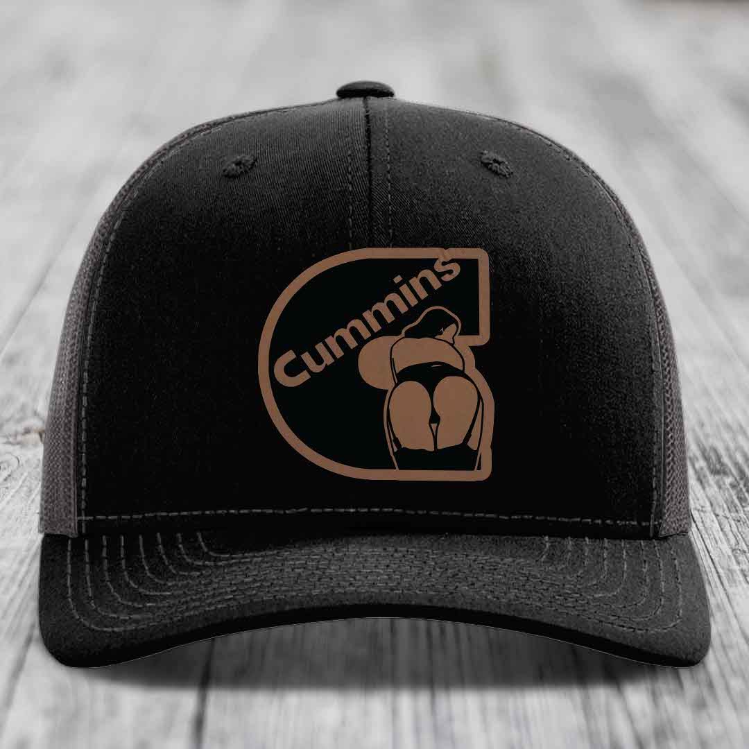 Black trucker hat with brown Cummins logo patch on front, white mesh back and stitching.