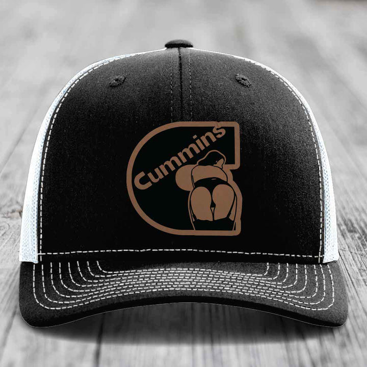 Black and white trucker hat with brown Cummins logo patch on front.