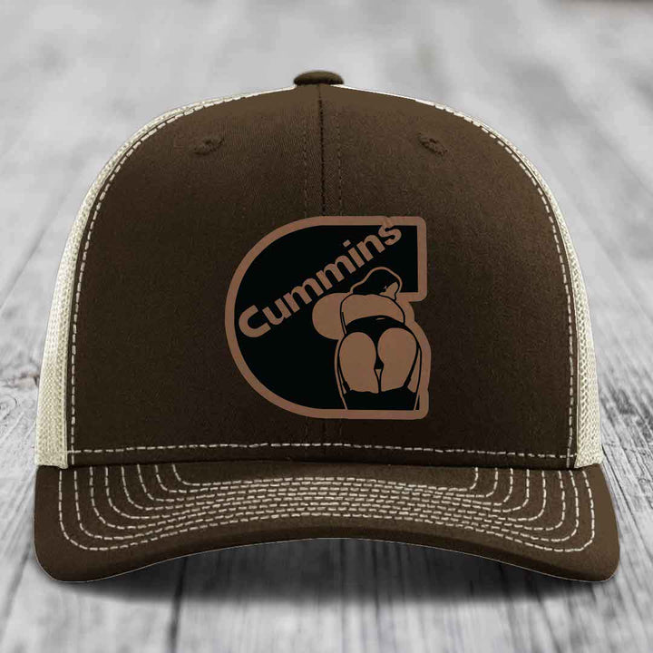 Tan trucker hat with black mesh back and Cummins logo patch on front.