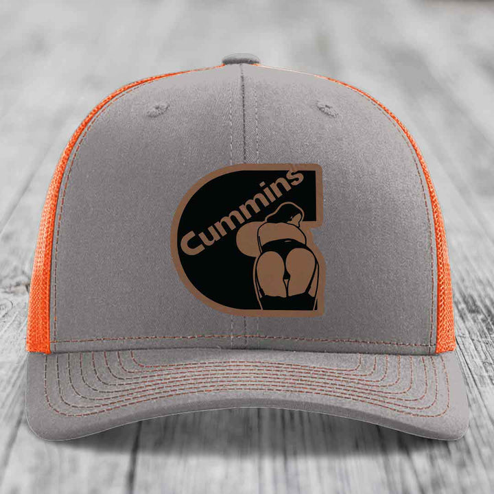 Grey trucker hat with pink mesh sides and a brown Cummins logo patch on front.