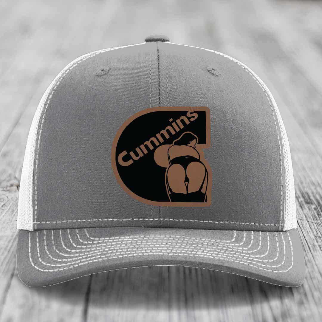 Pink trucker hat with black mesh back and a brown leatherette patch featuring the Cummins logo.