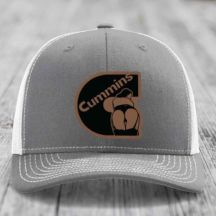 Pink trucker hat with black mesh back and a brown leatherette patch featuring the Cummins logo.