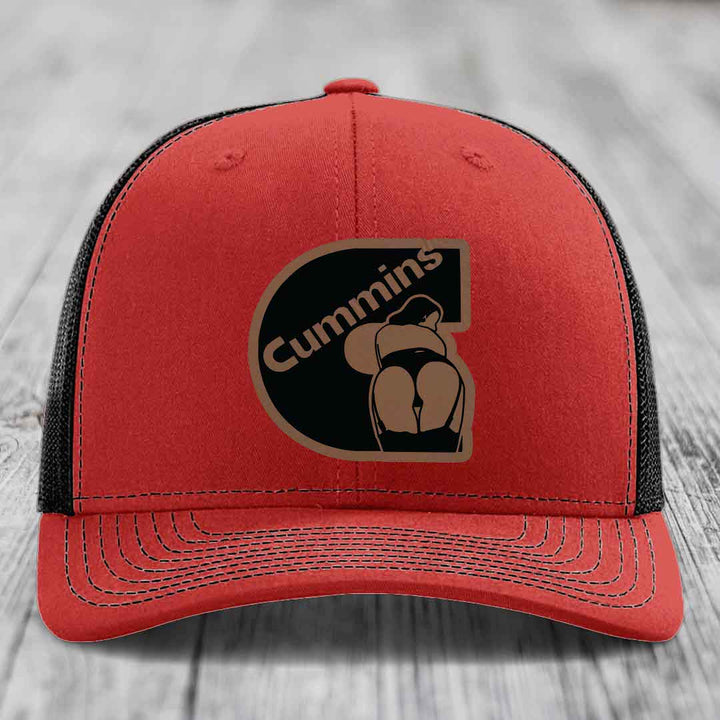 Blue trucker hat with black mesh back and brown Cummins logo patch on front.