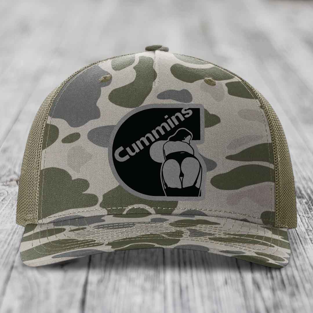 Camouflage trucker hat with black Cummins logo patch on front.