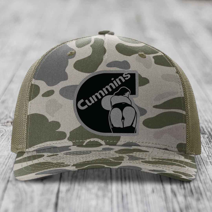 Camouflage trucker hat with black Cummins logo patch on front.