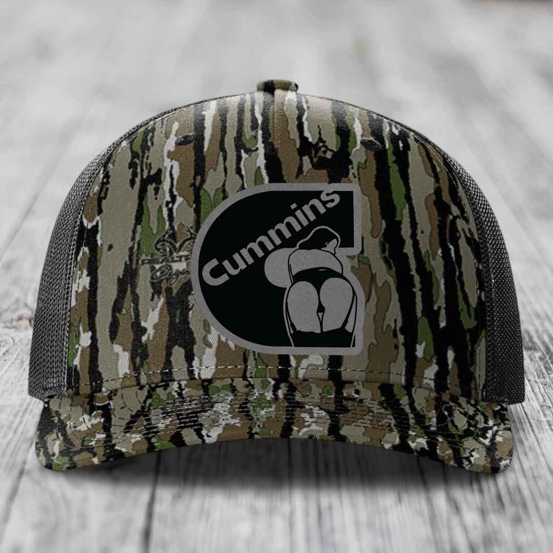 Black camouflage trucker hat with Cummins logo patch on front, resting on wooden surface.