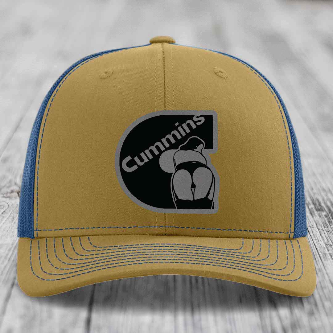 Black trucker hat with grey Cummins logo patch on front, resting on wooden surface.