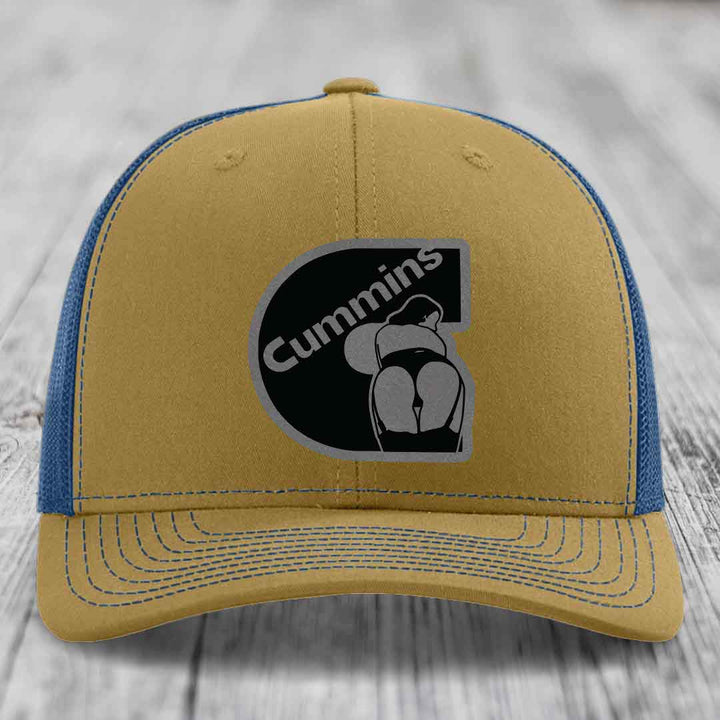 Black trucker hat with grey Cummins logo patch on front, resting on wooden surface.