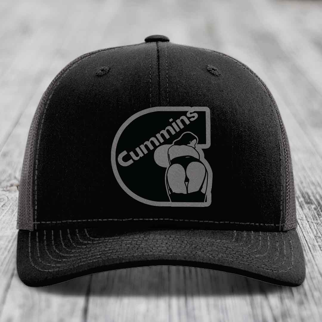 Black trucker hat with white stitching and a gray Cummins logo patch on front.