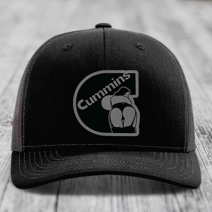 Black trucker hat with white stitching and a gray Cummins logo patch on front.