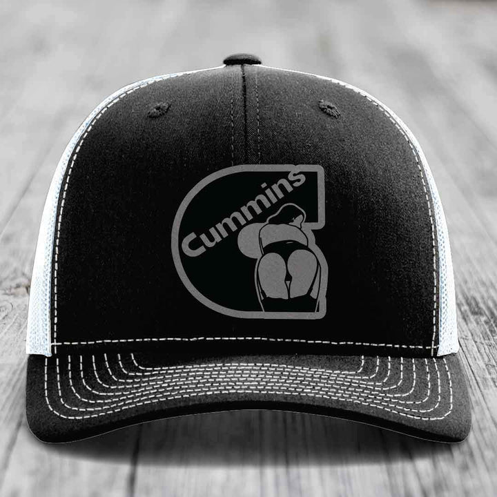 Black trucker hat with white mesh back and gray brim, featuring a gray Cummins logo patch on front.