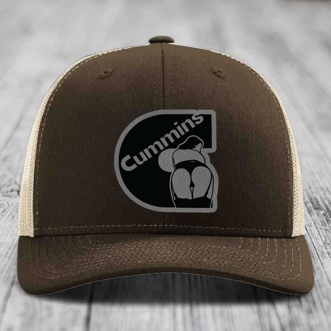 Green trucker hat with Cummins logo patch on front, resting on wooden surface.