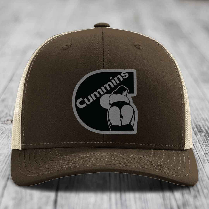 Green trucker hat with Cummins logo patch on front, resting on wooden surface.