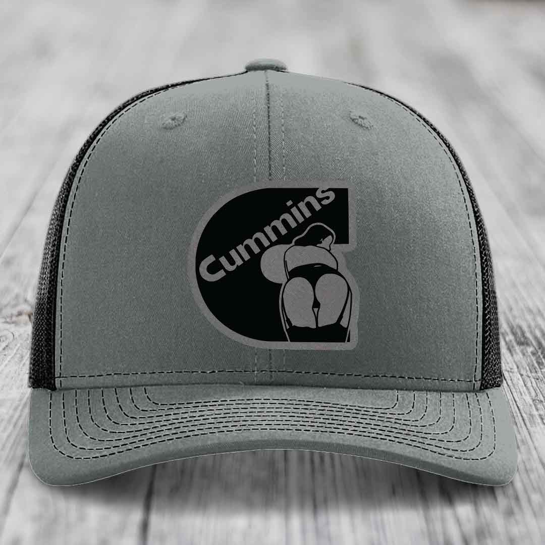 Grey trucker hat with black Cummins logo patch on front, white mesh back, and white stitching.