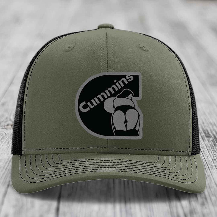 Black trucker hat with grey Cummins logo patch on front, resting on wooden surface.