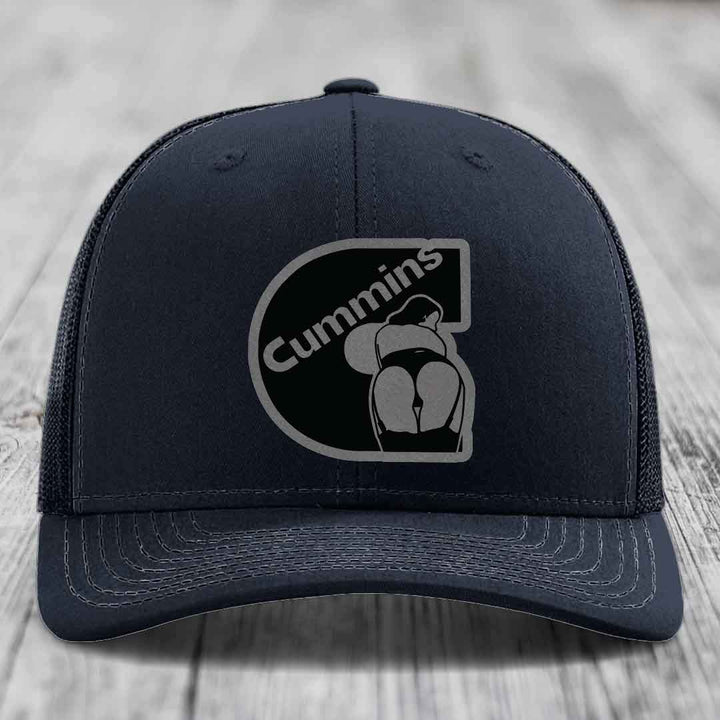 Purple trucker hat with black and grey Cummins logo patch on front.