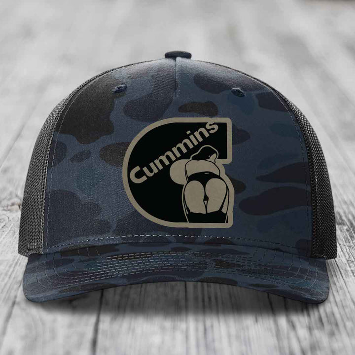 Camouflage trucker hat with black Cummins logo patch on front.