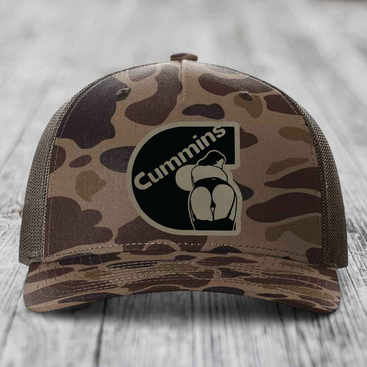 Camouflage trucker hat with black Cummins logo patch on front.
