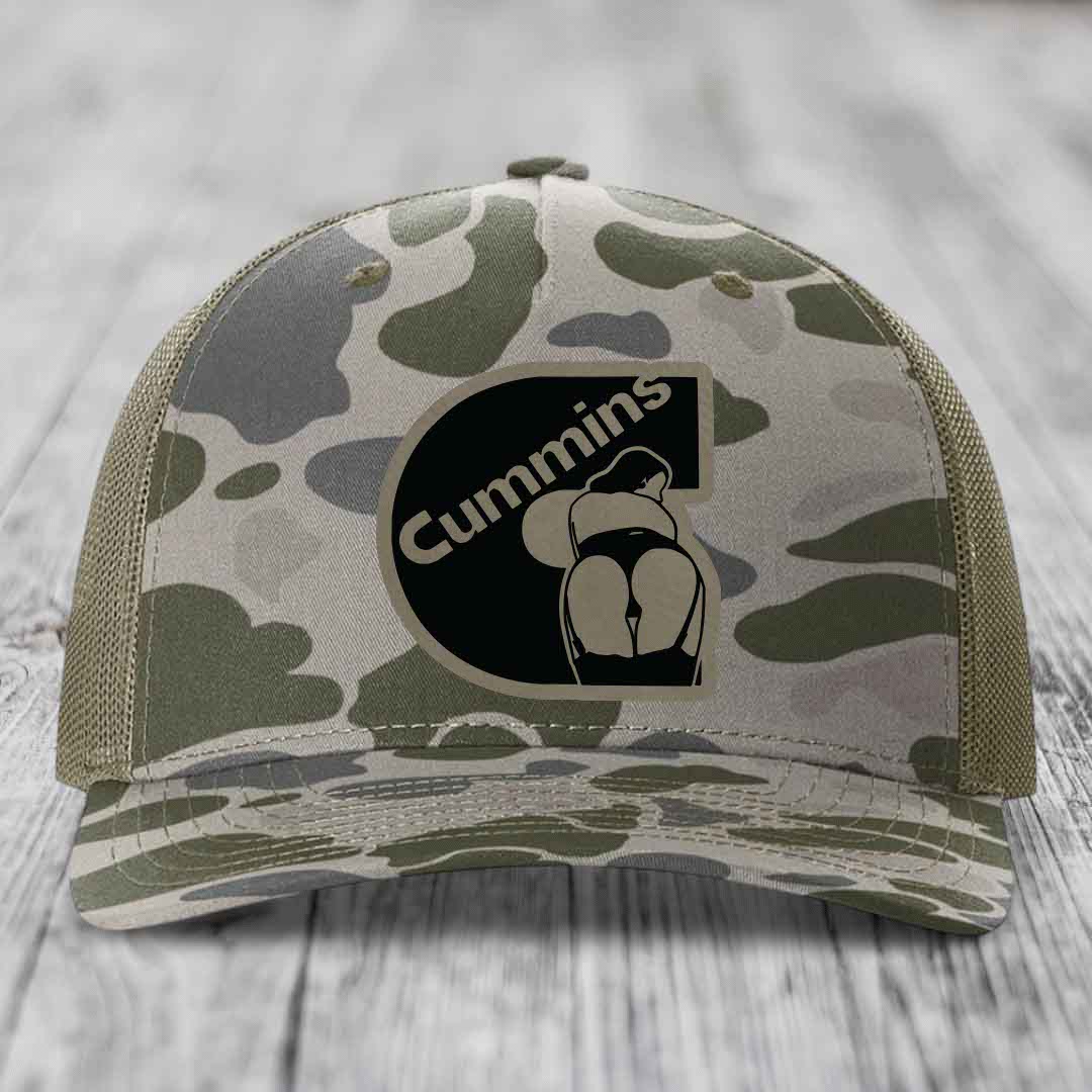 Camouflage trucker hat with black Cummins logo patch featuring a stylized engine graphic.