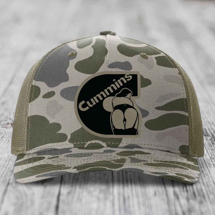 Camouflage trucker hat with black Cummins logo patch featuring a stylized engine graphic.