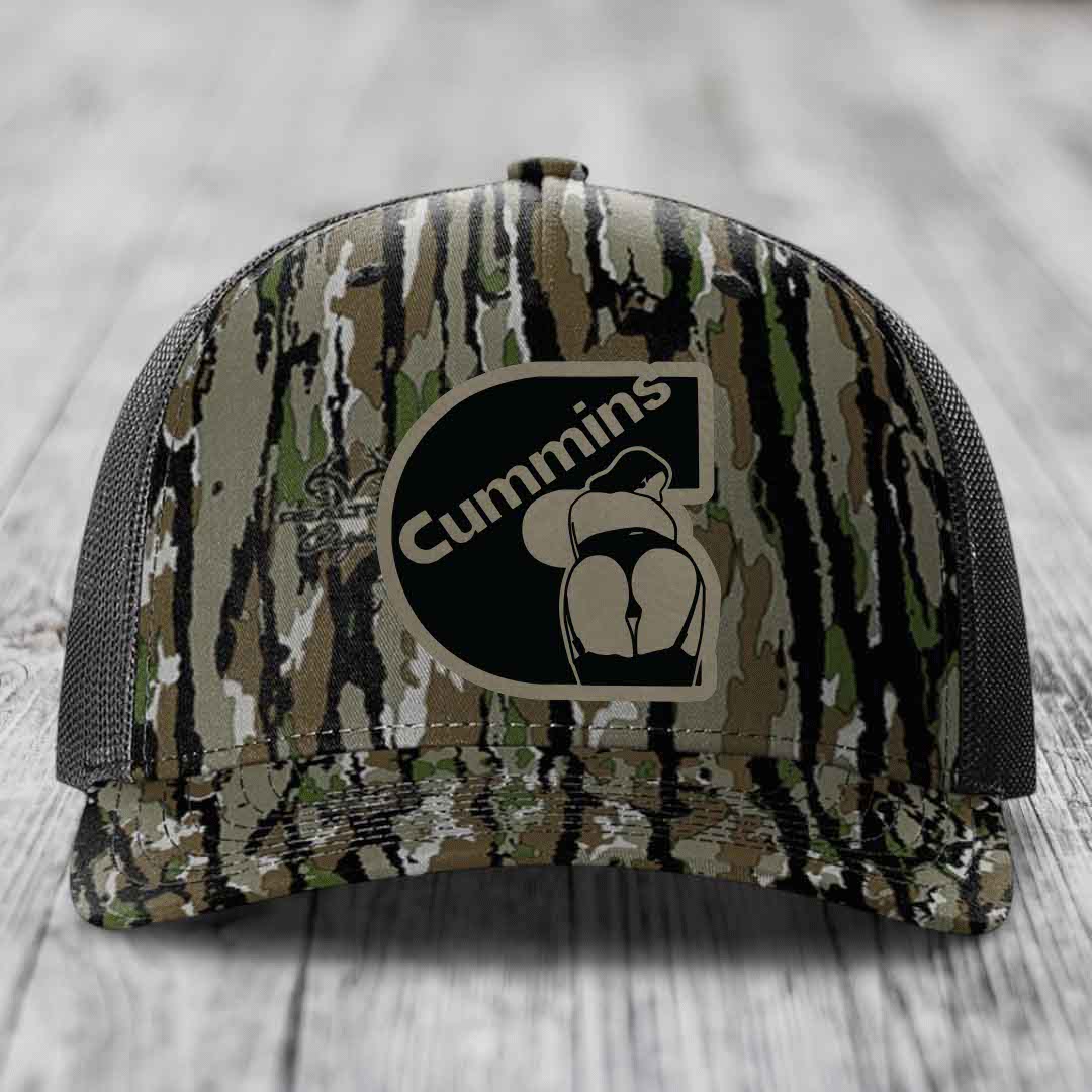 Black camouflage trucker hat with Cummins logo patch on front, resting on wooden surface.