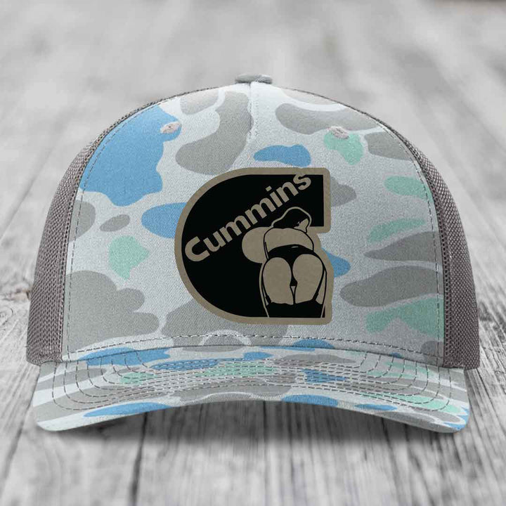 Camouflage trucker hat with Cummins logo patch featuring a stylized figure and text.