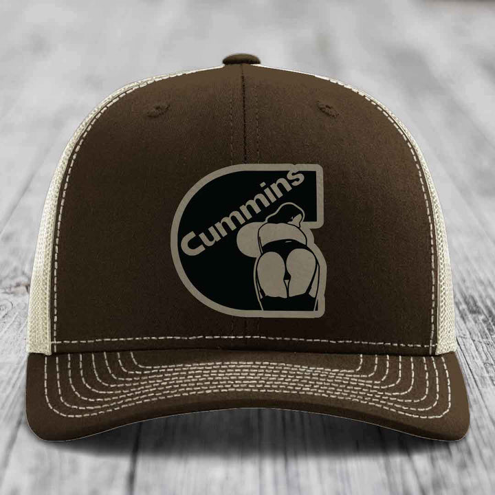 Tan trucker hat with black mesh back and Cummins logo patch on front.