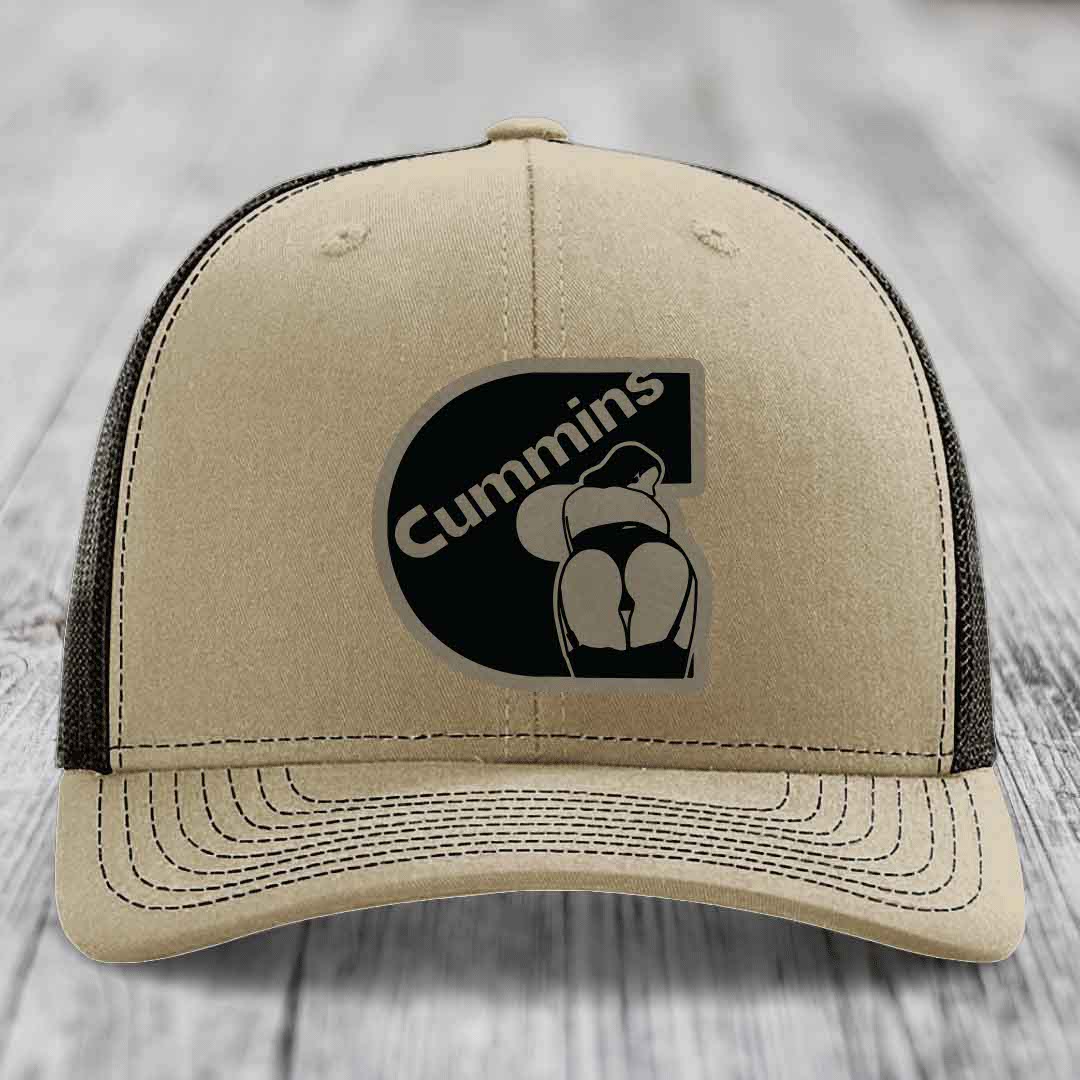Tan trucker hat with black Cummins logo patch on front, white mesh back and stitching.
