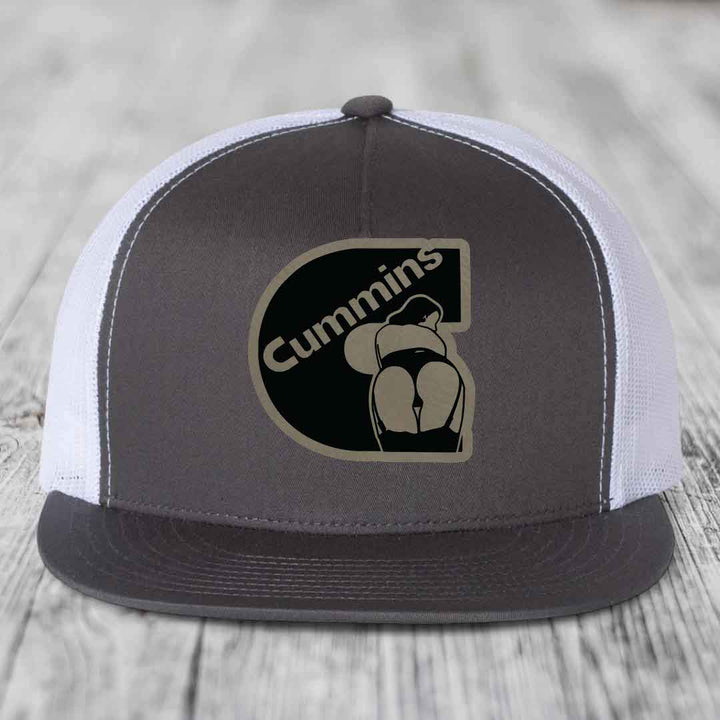 Black snapback trucker hat with brown Cummins logo patch featuring a stylized figure.