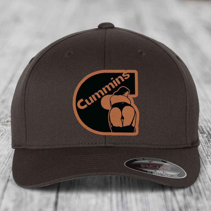 Dark brown Flexfit hat with Cummins logo patch featuring a stylized figure and orange border.