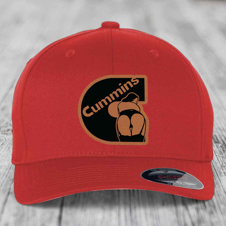 Red baseball cap with black and grey Cummins logo patch on front, featuring a stylized &