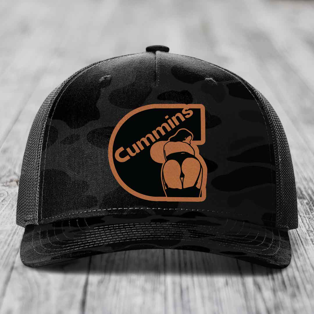 Camouflage trucker hat with Cummins logo patch on front, placed on wooden surface.