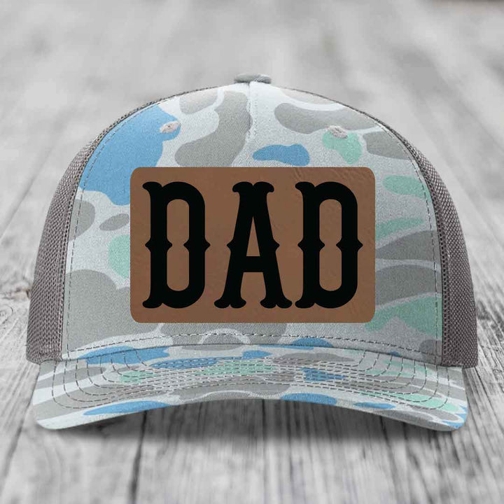 Black snapback hat with brown leather patch that says DAD in black letters.