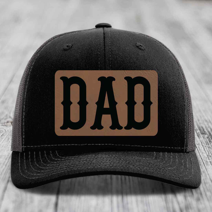 Black and white trucker hat with brown leather patch that says DAD in black letters.