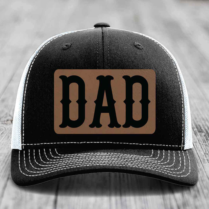 Black and white trucker hat with brown leather patch that says DAD in black letters.