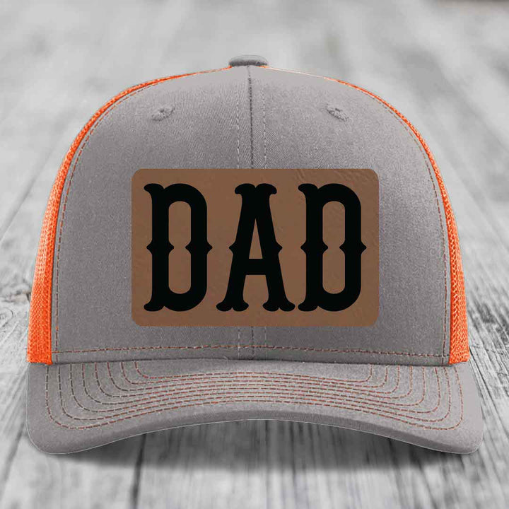Grey trucker hat with pink mesh sides and a brown leatherette patch that says &