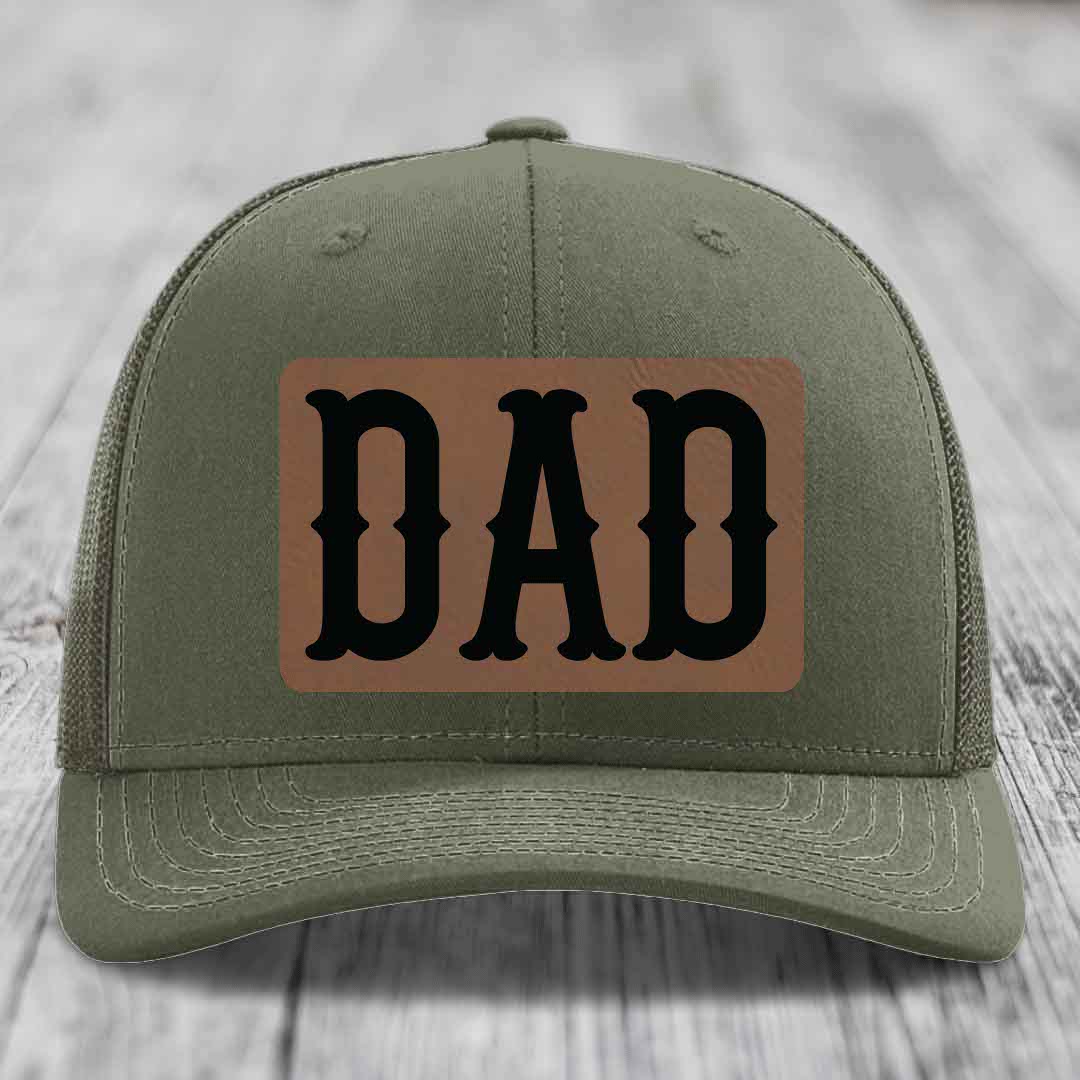 Olive green trucker hat with black mesh back and a brown leatherette patch that says DAD in black letters.